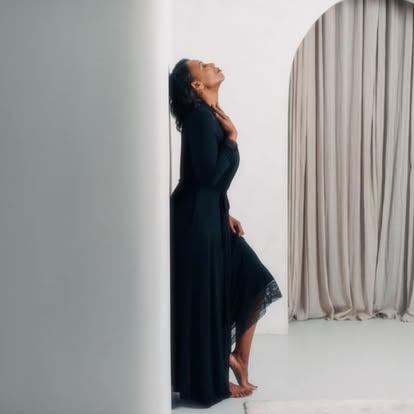 Charlene Salmon in a long black dress, leaning against a white wall beside a draped archway