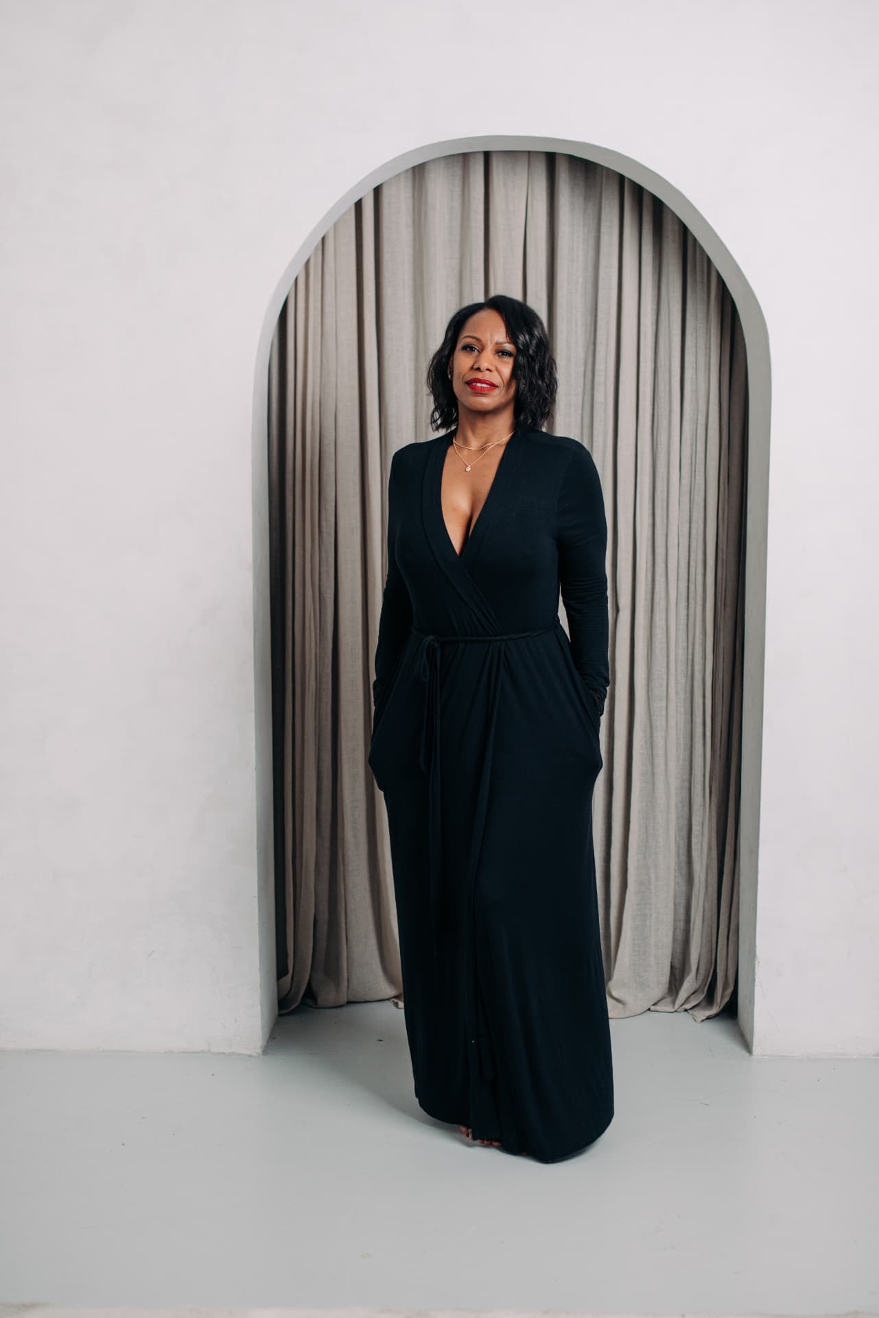 Charlene Salmon in a long black dress, standing in an arched doorway before linen curtains